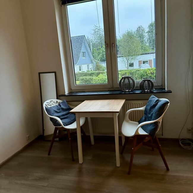 Ein Tisch mit zwei Stühlen vor einem Fenster des betreuten Wohnens von Neue Wege.